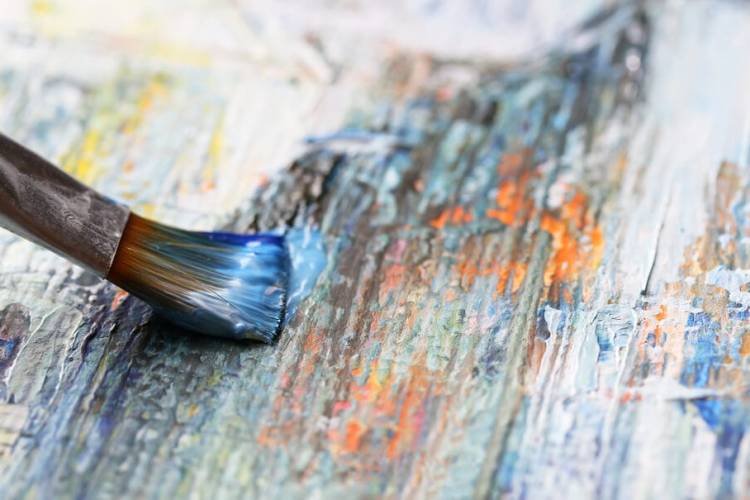 up-close view of a canvas with a paintbrush gliding across covered in blue paint