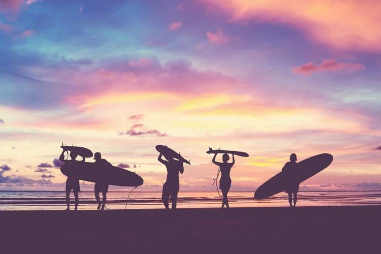 5 people running toward the ocean at sunset with surfboards in tow 