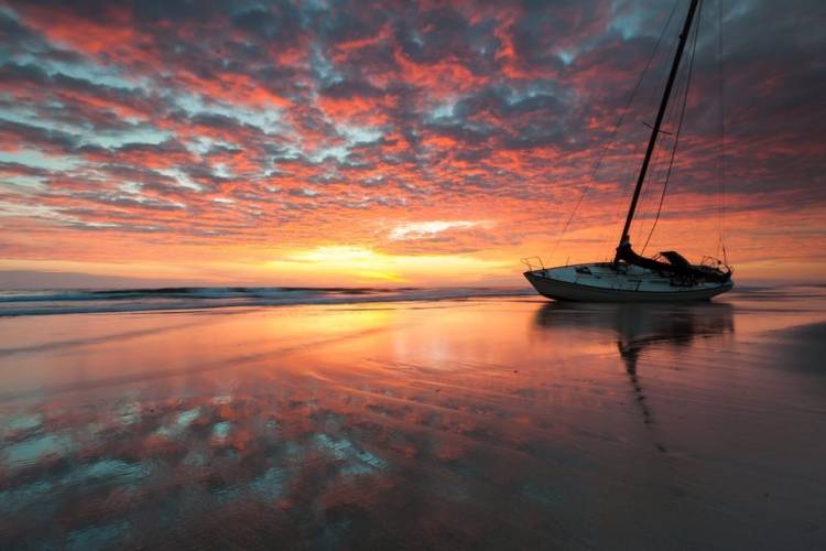 a sailboat washed onto the shore at sunset