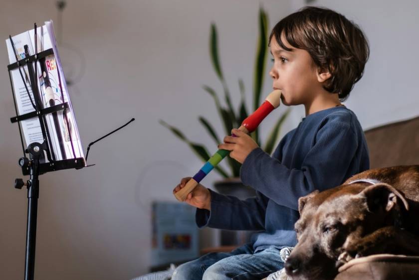 little boy playing a recorder while sitting on a couch next to a brown dog